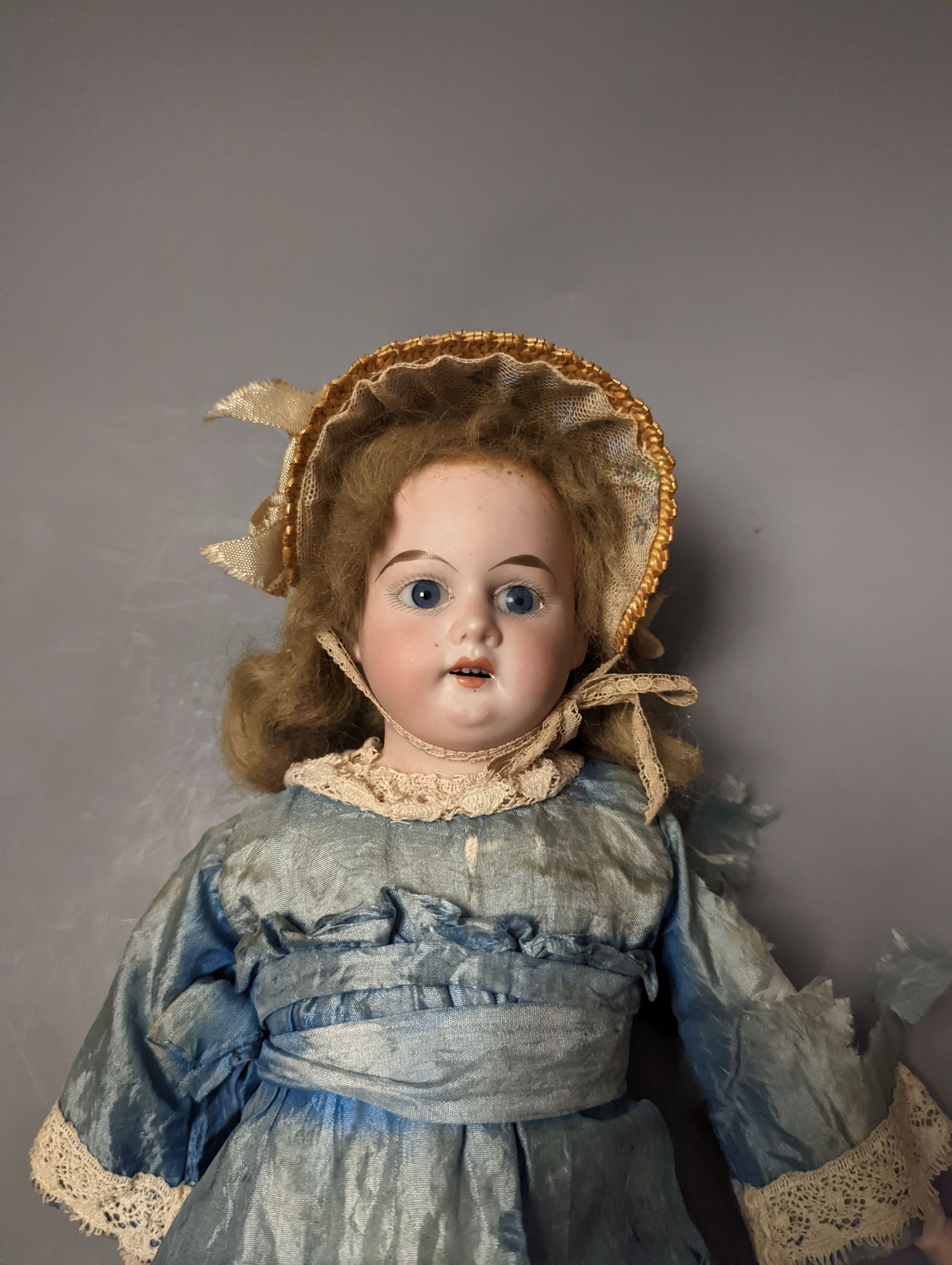 A German bisque headed doll, wearing a blue silk dress and straw bonnet, 42 cms high.